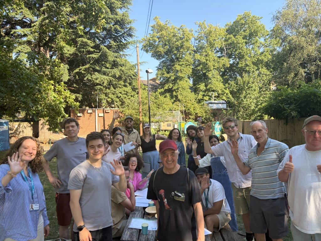 A group of tutors and Action Tutoring staff in a sunny park, smiling and waving at the camera.