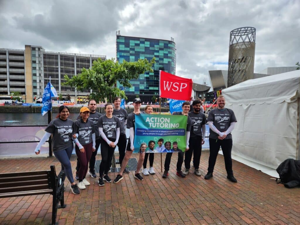 Group of ten people by the Salford Quays, holding a red WSP flag and an Action Tutoring banner.