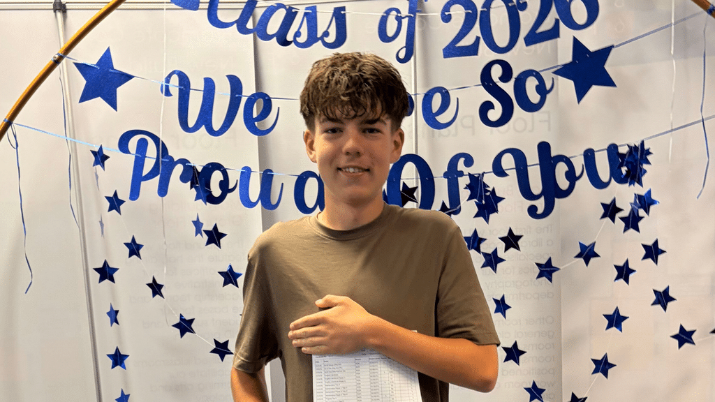Luke, tutored in maths, holds up GCSE results with a smile